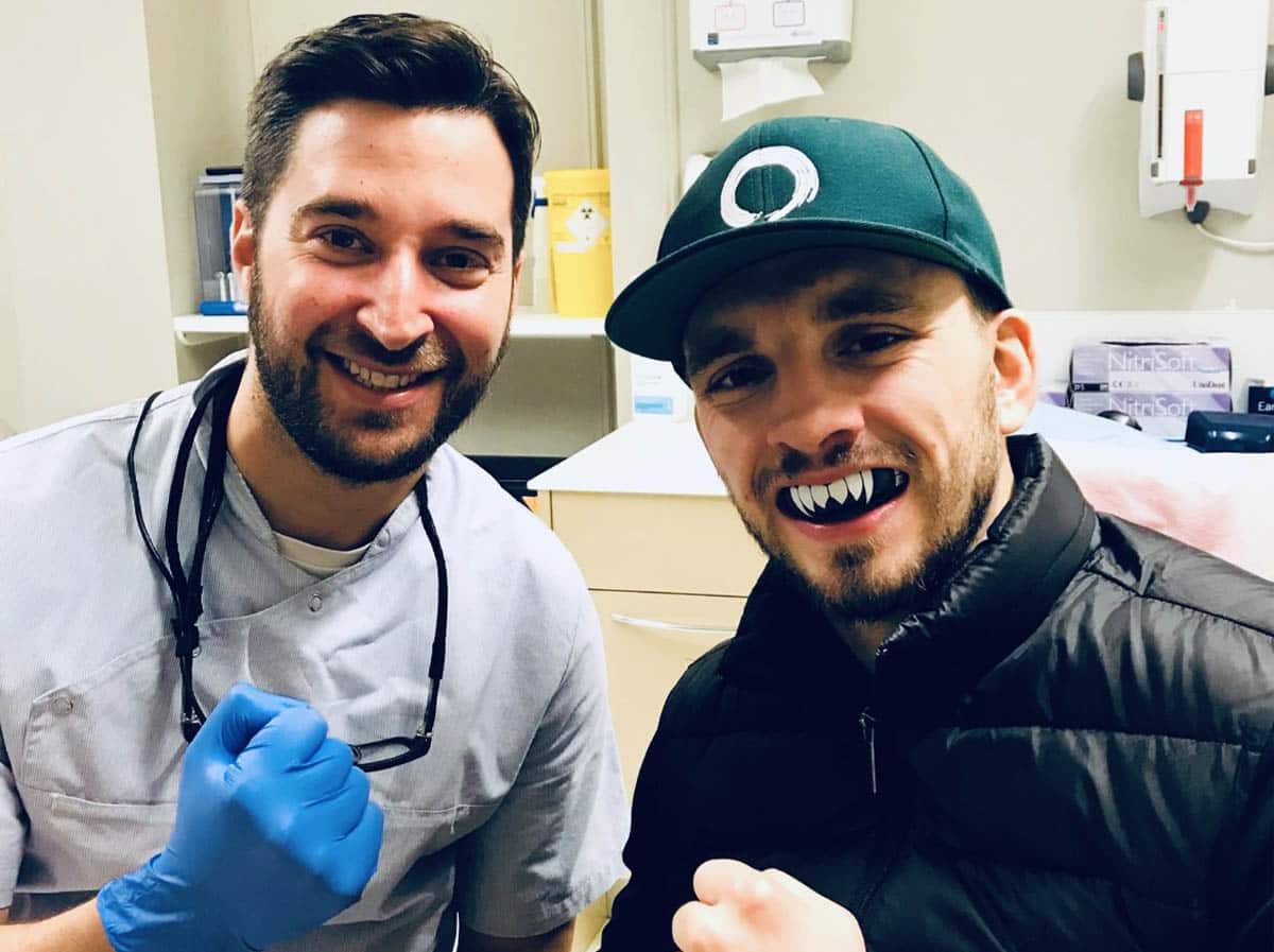 A dentist with a bard sports person, showcasing his mouth guard