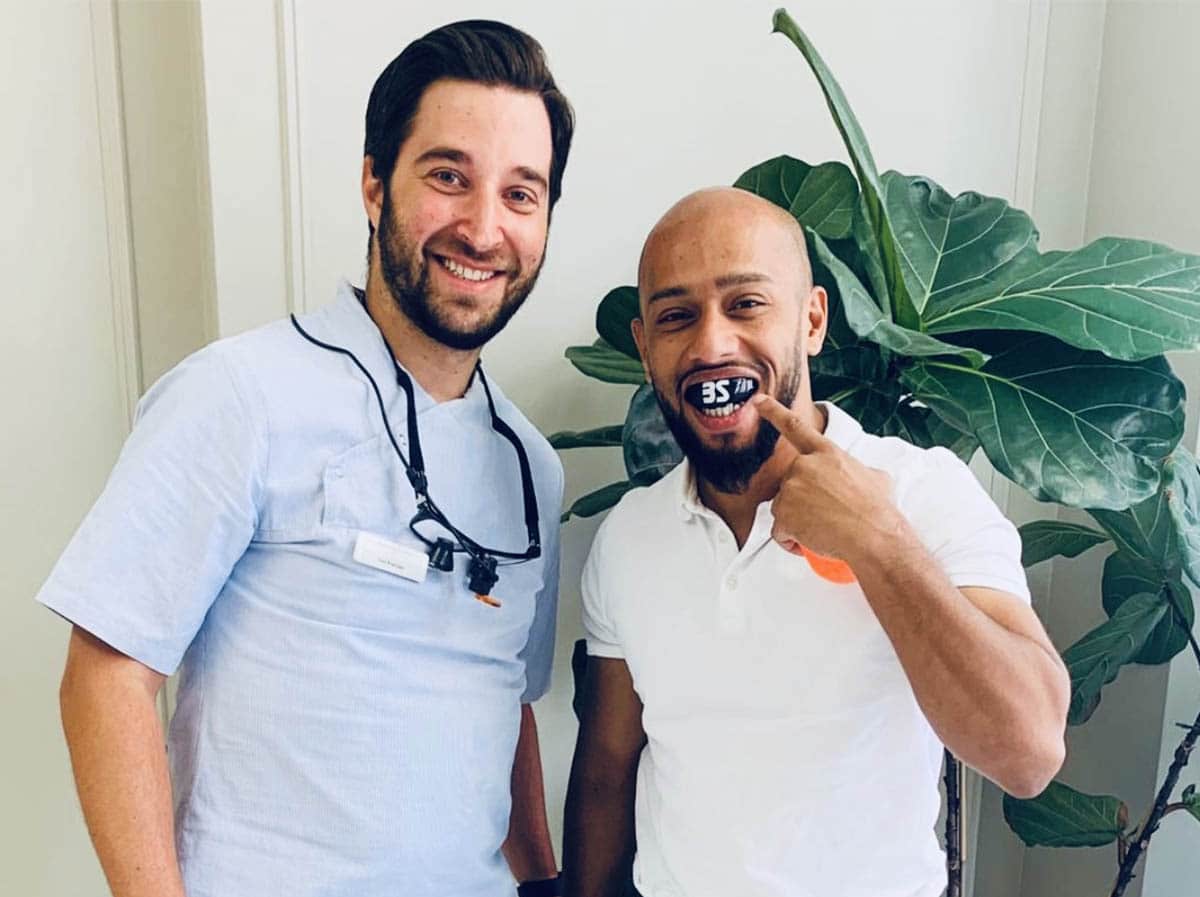 A dentist with a bard sports person, showcasing his mouth guard